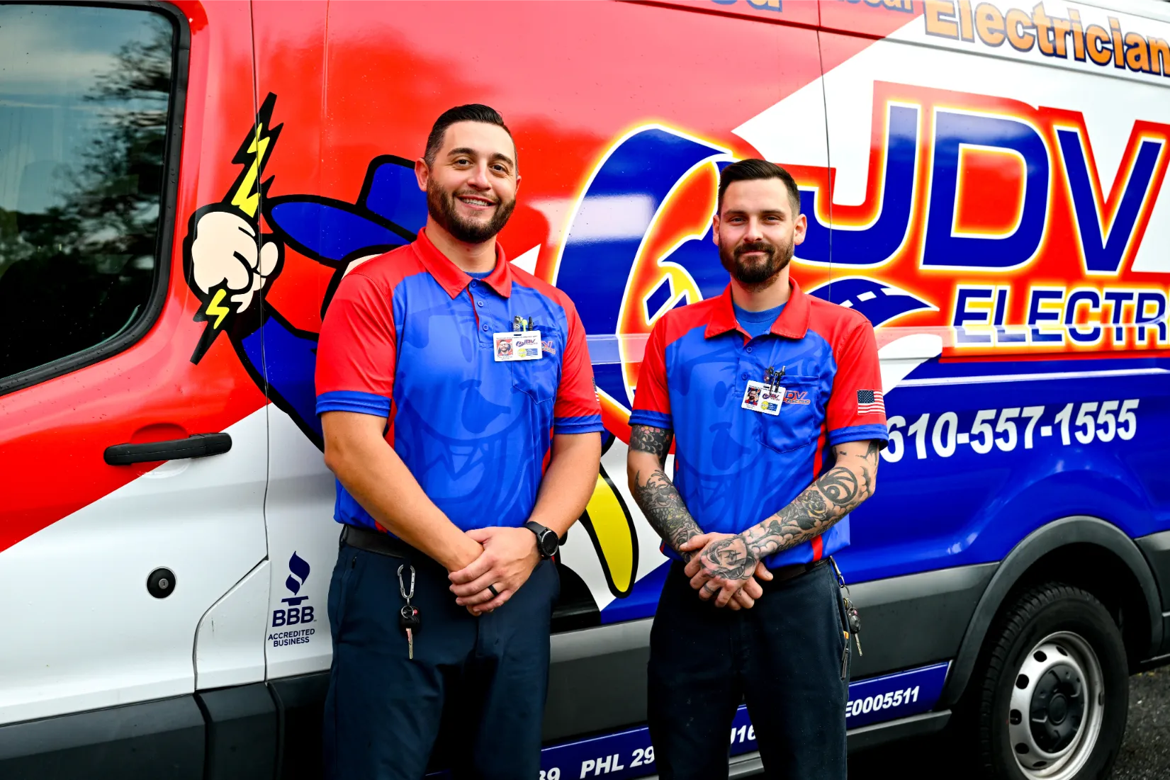 Six JDV Electric staff members standing side-by-side in a parking lot, with JDV service vans in background.